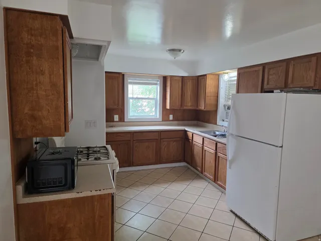 Kitchen with wood-finish cabinetry, light-toned countertops, and tile flooring
