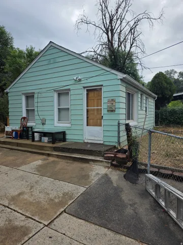 Single-story residence featuring light blue siding, a covered entry, and a chain-link fence