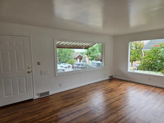 Hardwood-finish flooring, white paneled door, multiple windows, and white painted walls