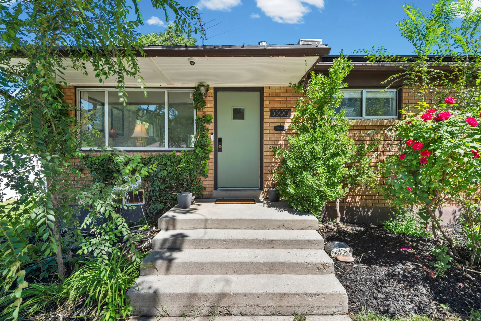 Brick exterior with a light green entry door, concrete steps, and established landscaping