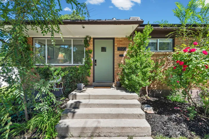 Brick exterior with a light green entry door, concrete steps, and established landscaping