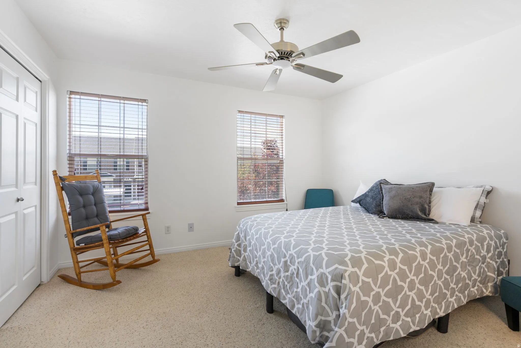 White painted walls, two windows with blinds, light-colored carpeting, and a ceiling fan with integrated lighting
