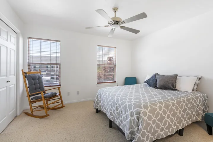 White painted walls, two windows with blinds, light-colored carpeting, and a ceiling fan with integrated lighting