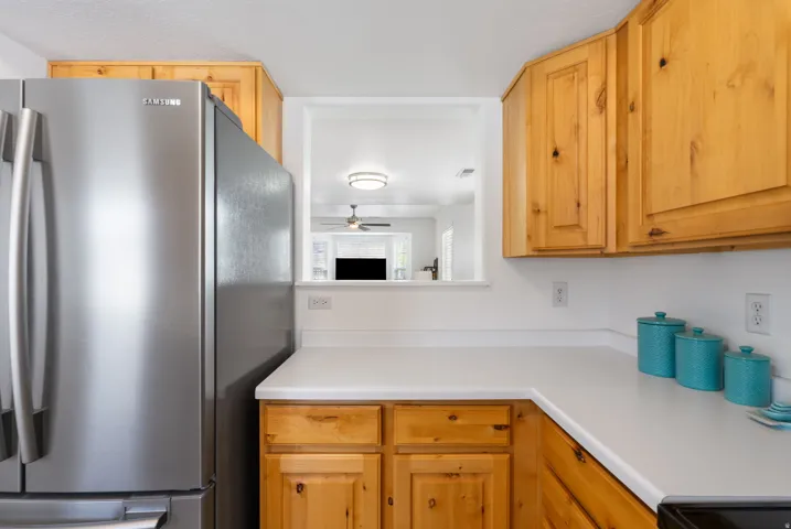 Efficient galley kitchen featuring warm wood cabinetry with knob hardware, stainless steel refrigerator, white countertops, and black cooktop