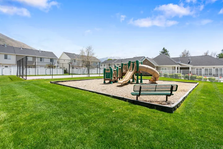 Expansive green space featuring a playground with slides, a basketball court with fencing, and perimeter white fencing