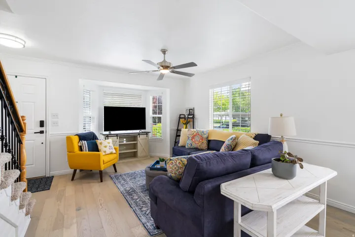 Bright, open-concept living space featuring engineered wood-finish flooring throughout, a ceiling fan with brushed metal finish, and abundant natural light from multiple windows