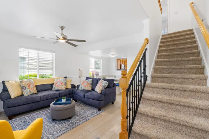 Carpeted staircase with wood railing, ceiling fan, wood-finish flooring, and horizontal window blinds