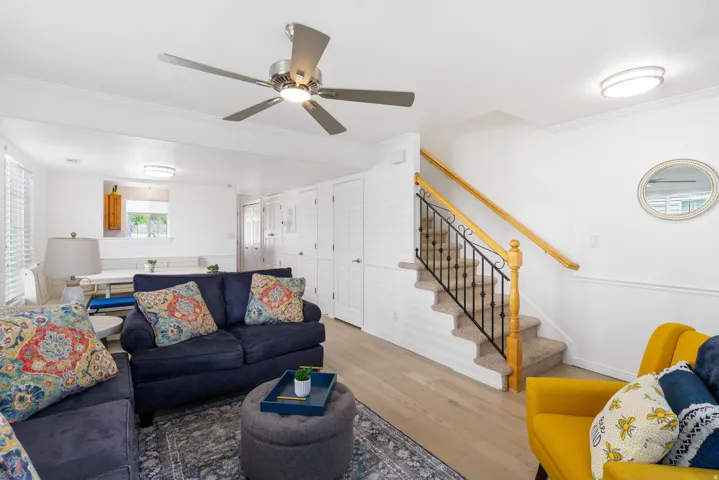 Wood-finish flooring, ceiling fan with integrated lighting, staircase with carpeted treads and wrought iron balusters, white wall paneling, and crown molding