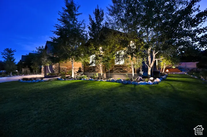 Manicured lawn with mature trees, stone-accented exterior, and integrated landscape lighting