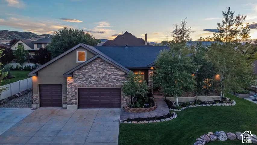 Exterior featuring stone veneer and stucco siding, a dark roof, two garage bays, a concrete driveway, and landscaped front yard