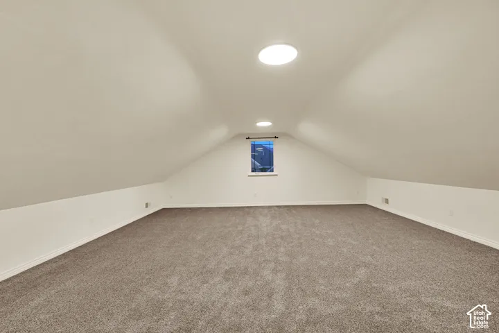 Sloped ceilings, window, two recessed circular light fixtures, and carpeted flooring