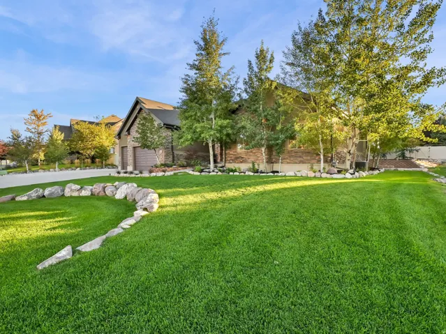 Expansive lawn with natural stone landscaping, mature trees, and a concrete driveway
