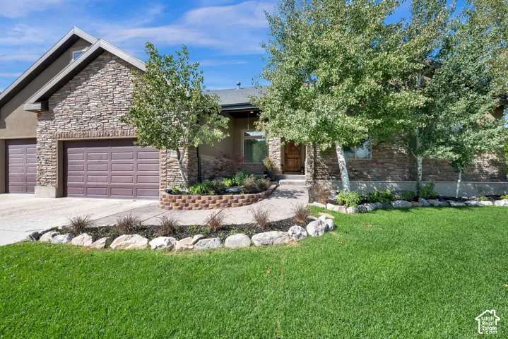 Stone veneer exterior with stucco accents, twin garage doors, mature landscaping, and a manicured lawn