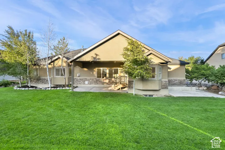 Expansive backyard featuring a manicured lawn, stone accents on the exterior, multiple mature trees, and a spacious patio area