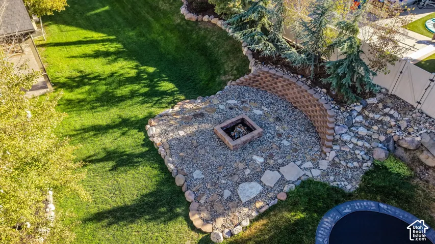Expansive outdoor space featuring a built-in fire pit with stone surround, a tiered retaining wall, and mature landscaping