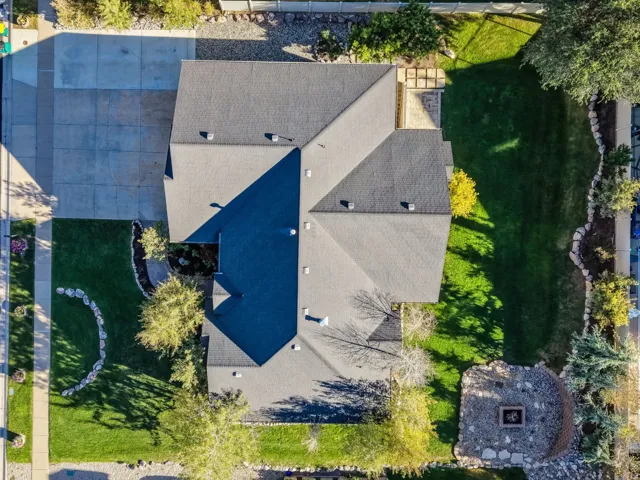 Expansive lot featuring a large grey asphalt shingle roof, concrete driveway, and manicured lawns