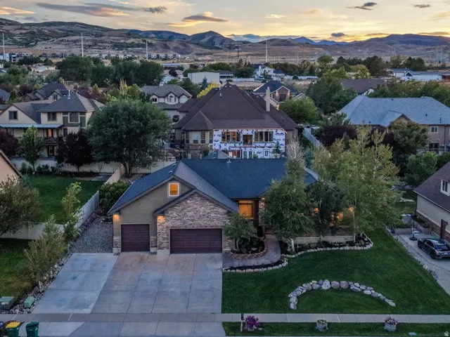 Stucco and stone facade with two attached garages, a concrete driveway, and a front lawn with established landscaping