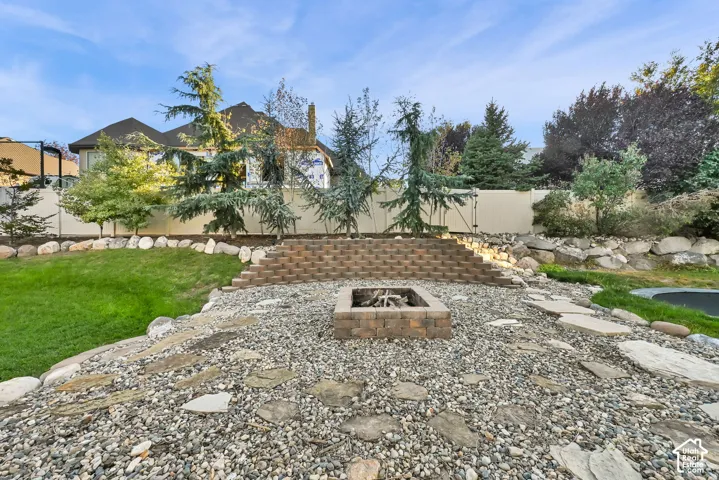 Landscaped backyard featuring a stone fire pit, tiered paver retaining wall, and a pebble and flagstone patio area