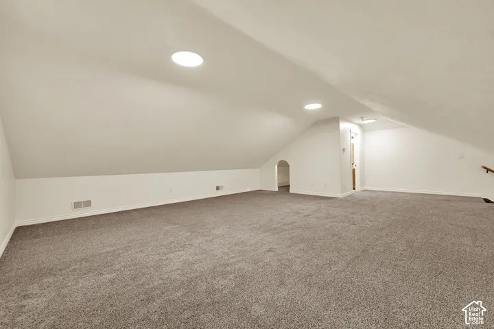 Expansive carpeted room featuring a sloped ceiling, recessed lighting, and wall-mounted handrail