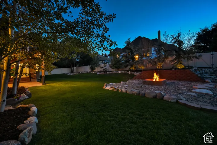 Expansive backyard featuring a manicured lawn, established trees, and a stone-bordered fire pit area