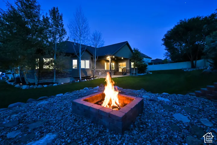 Expansive backyard featuring a built-in fire pit, stone-accented exterior, and mature trees
