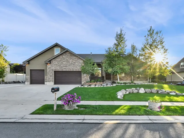 Stucco and stone exterior, two-car garage, manicured lawn, established trees, and a decorative rock border