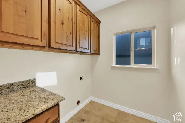 Wood-finish upper cabinetry, speckled countertop, tile flooring, and a single window