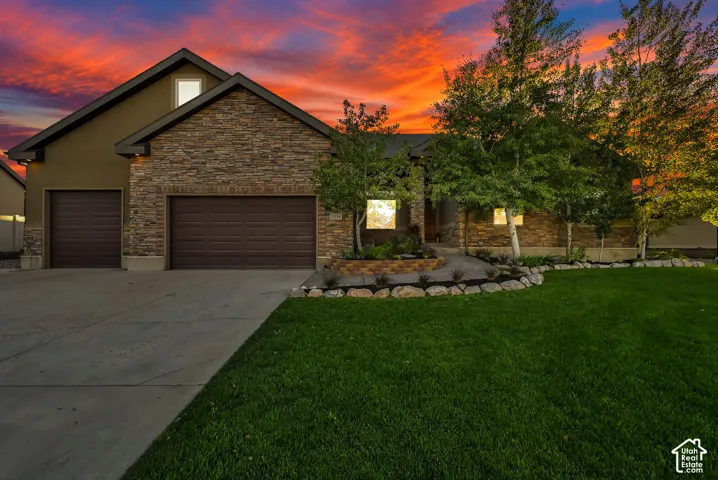 Stone and stucco exterior, two-car garage, concrete driveway, front yard with mature trees, and landscaped rock beds