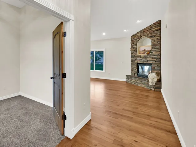 Hardwood flooring, stone-clad corner fireplace with recessed niche, recessed lighting, and vaulted ceiling