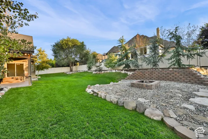 Expansive lawn, tiered retaining wall, built-in fire pit, stone hardscaping, covered patio