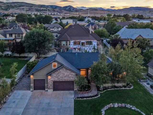 Exterior featuring a stone and stucco facade, an attached two-car garage, mature landscaping, and a paved driveway