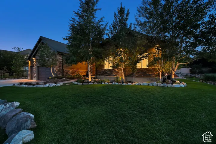 Stone facade, stucco accents, prominent garage, mature landscaping, and exterior illumination
