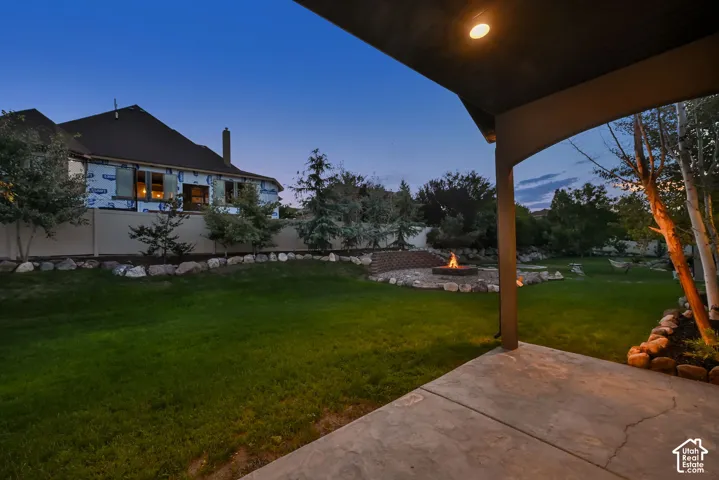 Expansive backyard featuring a concrete patio, a built-in fire pit, and mature trees