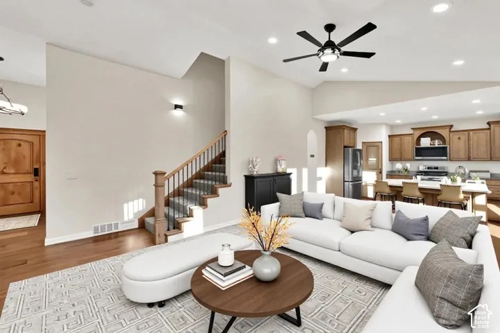 Vaulted ceiling with a contemporary ceiling fan, wood-finish flooring, staircase with wood newel posts and metal spindles, recessed lighting, and kitchen with wood cabinetry