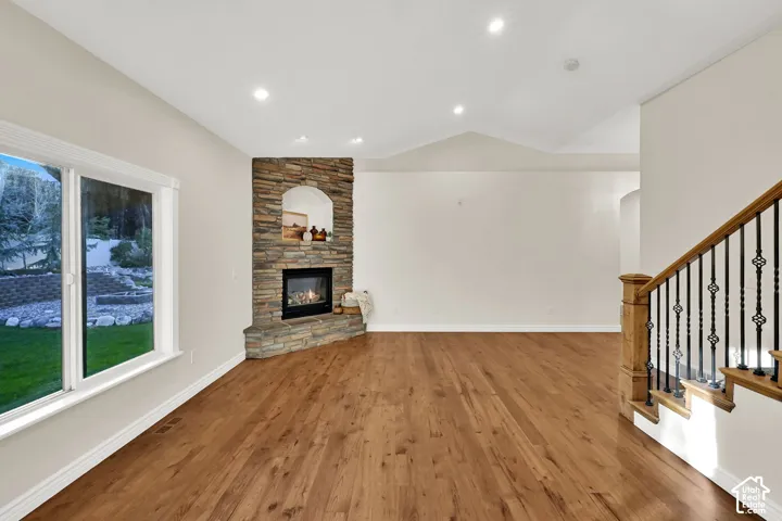Wood-finish flooring, recessed lighting, and a stone-clad fireplace with an arched niche