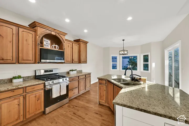 Kitchen featuring natural wood cabinetry, granite countertops, stainless steel appliances, a kitchen island with a double basin sink, and wood-finish flooring