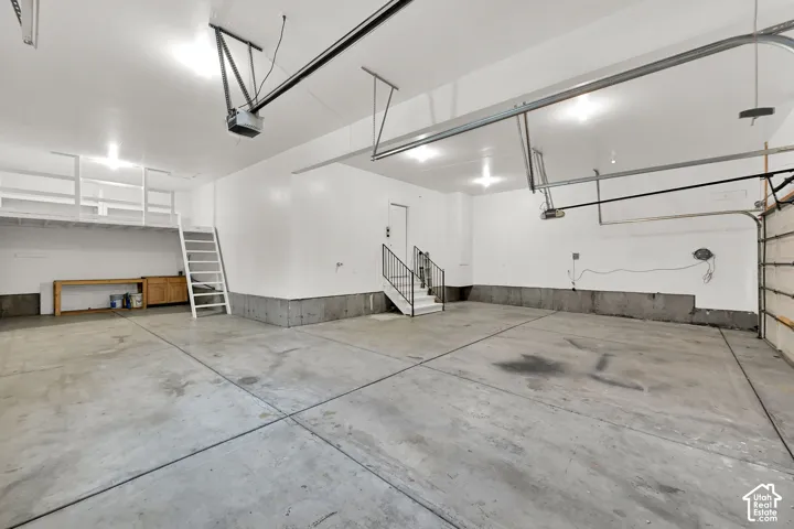 Spacious garage featuring concrete flooring, overhead storage shelving, and a built-in workbench with cabinetry