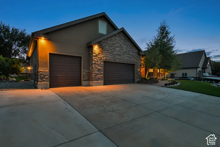 Stucco and stone exterior featuring two garage doors, outdoor lighting, and a concrete driveway