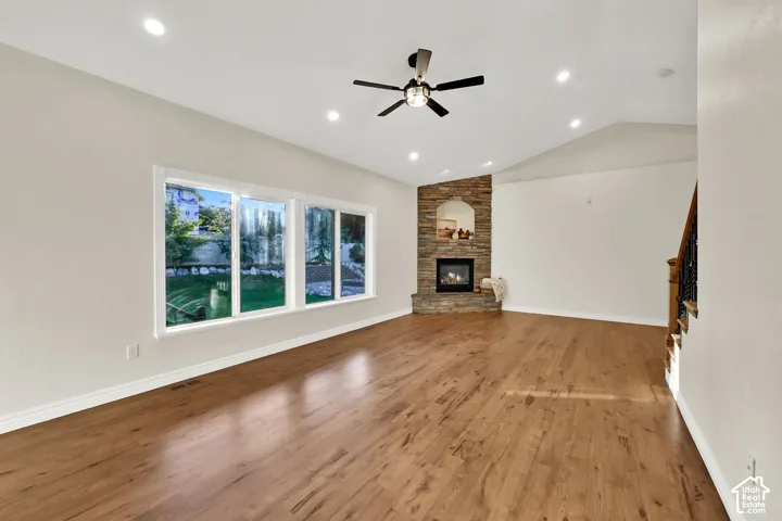 Spacious room featuring wood-finish flooring, a stone-clad corner fireplace, and a vaulted ceiling with recessed lighting