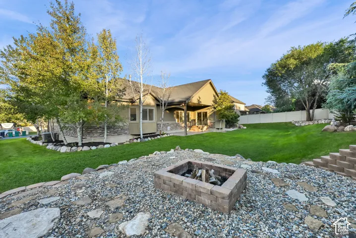 Expansive backyard featuring a built-in fire pit, terraced landscaping, a covered patio, and a manicured lawn