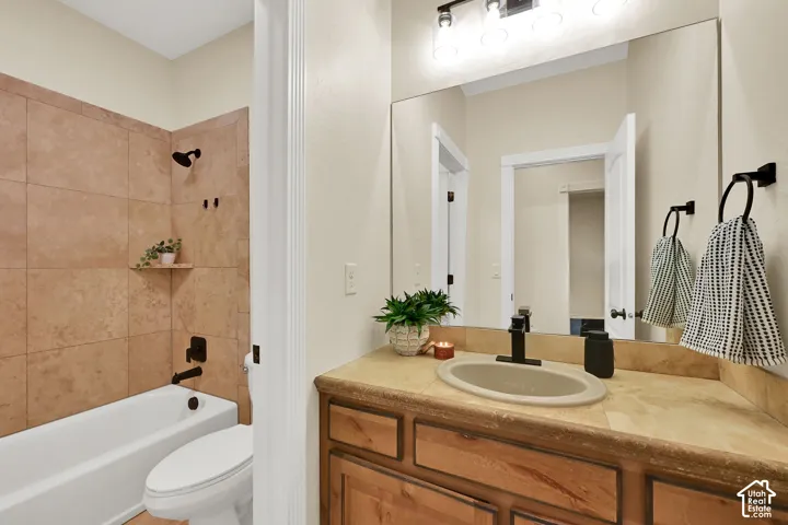 Full vanity mirror, wood-finish cabinetry, countertop with integrated sink, tub/shower combination, and tiled shower surround