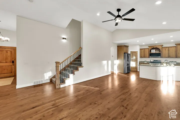 Vaulted ceilings, wood-finish flooring, staircase with metal balusters, recessed lighting, and kitchen with wood cabinetry