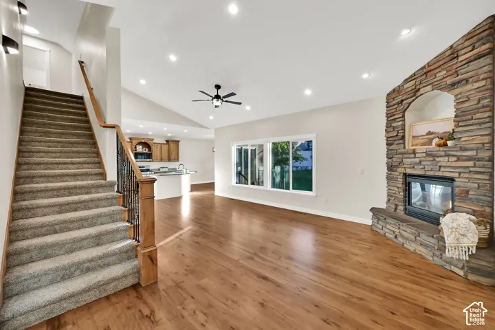 Stone-clad fireplace with arched niche, wood-finish flooring, vaulted ceiling, recessed lighting, and a wood railing with wrought iron balusters