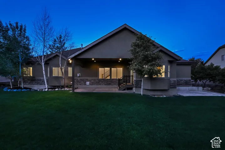 Rear exterior featuring a covered patio, extensive grass lawn, and stone accents