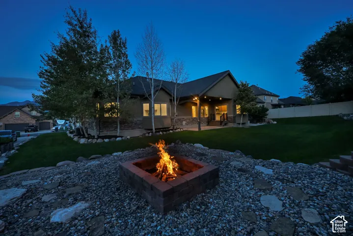 Expansive backyard featuring a stone-clad fire pit, gravel and stone landscaping, a manicured lawn, and a covered patio