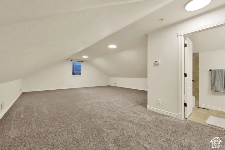 Expansive carpeted area with sloped ceilings, recessed lighting, and a window