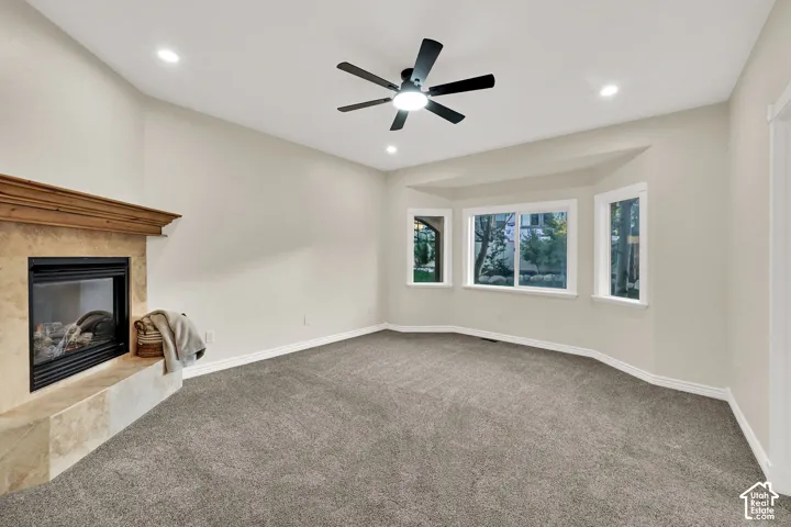 Fireplace with a wood mantle and stone surround, bay windows, vaulted ceiling, recessed lighting, and a ceiling fan