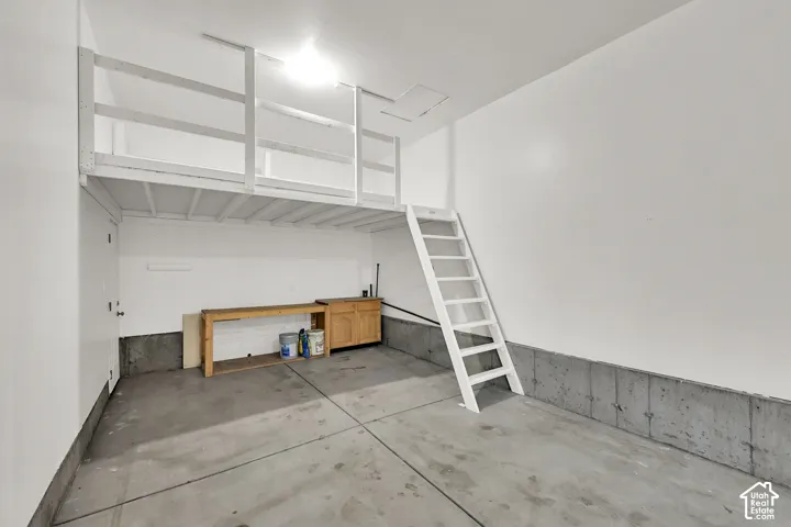 Attached garage featuring a concrete floor, built-in overhead storage loft with ladder access, and a workbench area