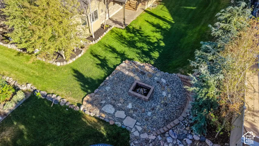 Manicured lawn, mature trees, stone-edged garden beds, fire pit with stone and flagstone surround, and established landscaping