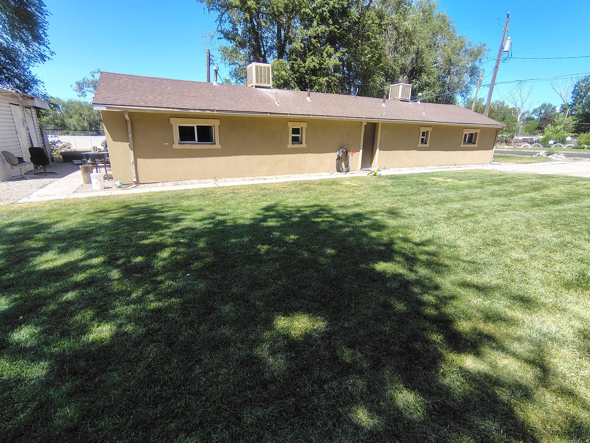 Stucco exterior with multiple windows, a composite shingle roof, and a gravel patio area